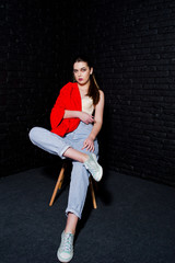 Stylish brunette girl on red jacket against studio black brick wall.