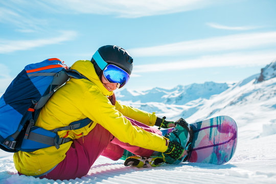 Image of sporty woman in helmet sitting on snow with snowboard