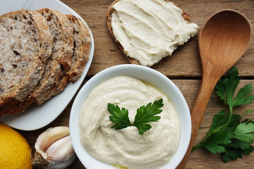 Bawl of hummus with homemade brad, garlic, lemon  and parsley on wooden table, oriental cuisine
