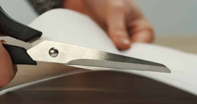 Close up of the woman's hand holding scissors and cutting a white sheet of paper. Macro