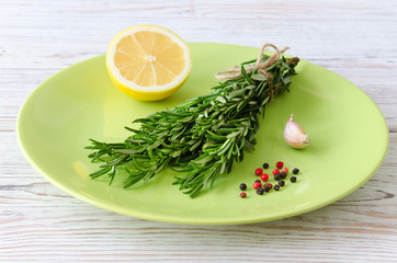 Bunch of rosemary with spices and lemon on green plate