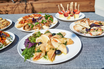 Delicious thin pancakes with salmon, dill and olives on white plate on dinner table outdoors, free space. Russian cuisine. Maslenitsa. Rolls of thin pancakes with smoked salmon