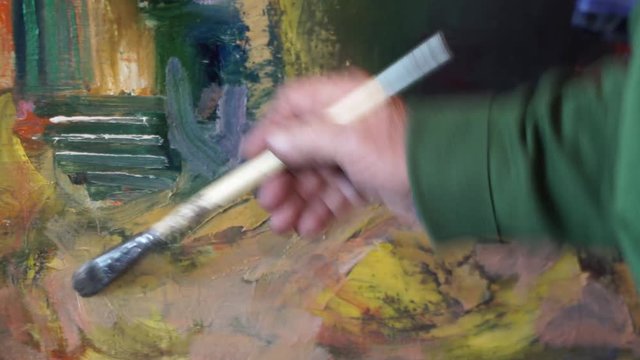 The old artist paints his painting in a workshop of oil painting