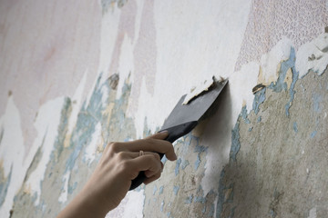 hand with a spatula cleans the wall from Wallpaper