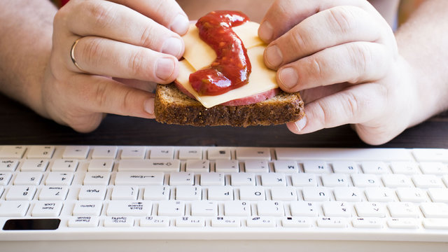 Fat Man Holding A Sandwich At The Table In Front Of The Keyboard