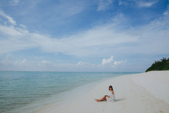 beautiful young woman in sunglasses and dress resting on sandy beach at Ukulhas island, Maldives
