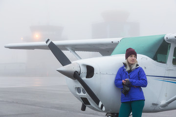 Young Caucasian Female Student Pilot is standing in front of a Single Engine Airplane at the...
