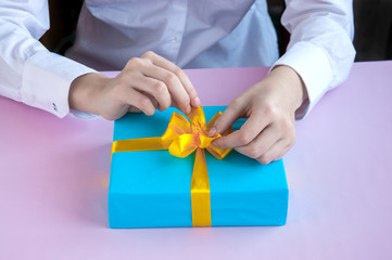 Female hands tie a gift with a yellow ribbon on a pink background