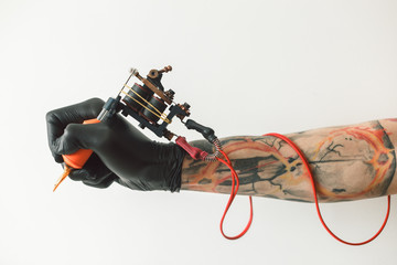 Man's hand holding tattoo machine on white background. the red wires