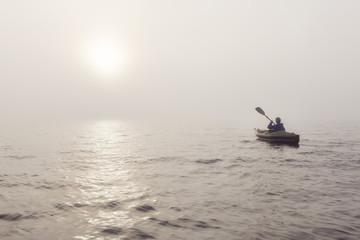Naklejka premium Girl kayaking on an inflatable kayak in Howe Sound during a fog covered winter sunset. Taken in West Vancouver, BC, Canada.