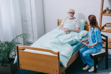 Old man patient and nurse discussing news from newspaper - obrazy, fototapety, plakaty