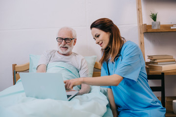 Nurse pointing at laptop in senior patient hands