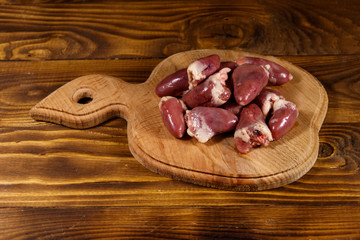 Raw chicken hearts on cutting board on wooden table