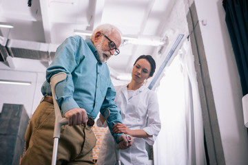 Doctor supporting male patient with crutches