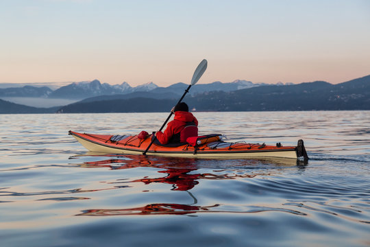 Man on Sea Kayak is kayaking during a vibrant winter sunset. Taken near Jericho Beach, Vancouver, BC, Canada.