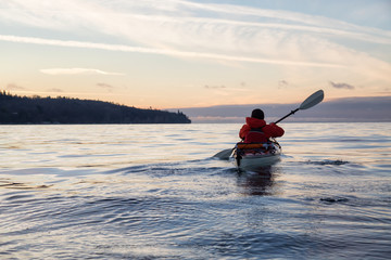 Fototapeta na wymiar Man on Sea Kayak is kayaking during a vibrant winter sunset. Taken near Jericho Beach, Vancouver, BC, Canada.