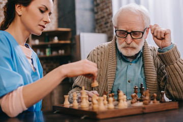 Nurse and senior man playing chess - obrazy, fototapety, plakaty