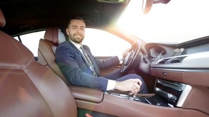 View from the side confident businessman sits at the wheel of a 