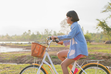 Obraz premium young asian woman riding bicycle at park with sunset