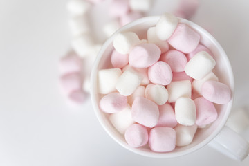 Fototapeta na wymiar White cup full of white and pink mini marshmallows on white background