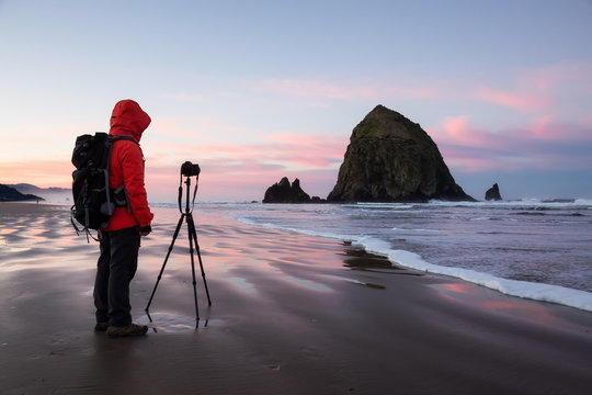 Photographer taking picture of the beautiful sunrise on Pacific Ocean Coast. Taken at Canon Beach, Oregon, America