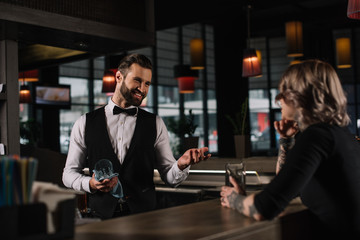 smiling bartender cleaning glass and talking with female visitor - obrazy, fototapety, plakaty