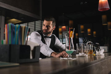 handsome bartender leaning on bar counter and looking away