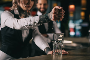 tattooed bartender squeezing out lemon juice into glass at bar