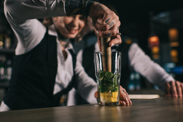 tattooed female bartender showing colleague how to prepare drink at bar
