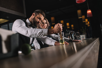 male bartender showing colleague how to prepare drink at bar