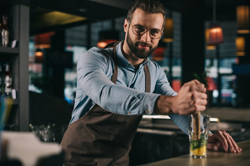 handsome bartender preparing alcohol drink and looking at camera