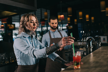 tattooed bartender putting plastic straws in glass with alcohol drink at bar