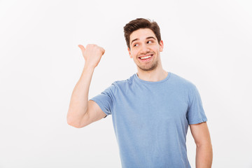 Fototapeta premium Closeup image of man with shining smile in casual clothing pointing finger aside on copyspace text or product, isolated over white background