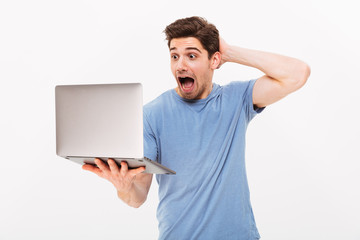 Excited masculine man in casual t-shirt expressing delight while looking on screen of silver laptop in hand, isolated over white background