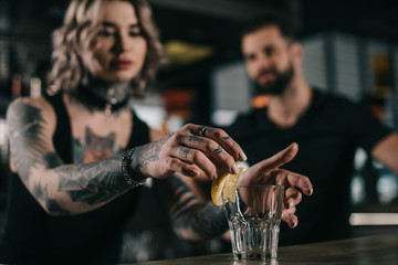 bartender putting piece of lemon in glass at bar