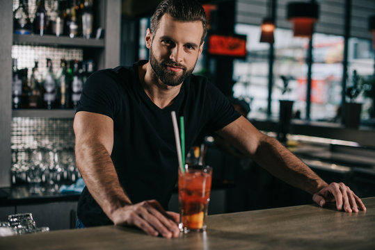 handsome barman standing with alcohol drink at bar counter