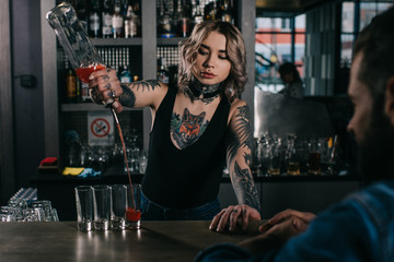 tattooed bartender making shot drinks for man at bar