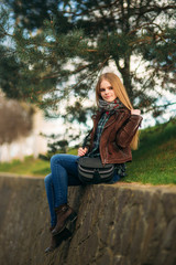 A beautiful girl is walking along the embankment. Blond hair and brown jacket. Spring