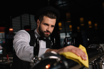 Fototapeta na wymiar handsome bartender cleaning beer taps with rag