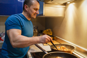 The man in the kitchen is cooking at home at the wok