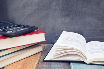 Books and calculator on a black chalkboard, wooden table