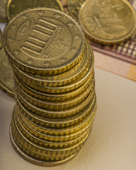 pile of fifty euro cents lie on a paper bill of fifty euros.