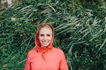 Naklejka premium portrait of a smiling young woman in a pink jacket with a hood outdoor on a background of green plants
