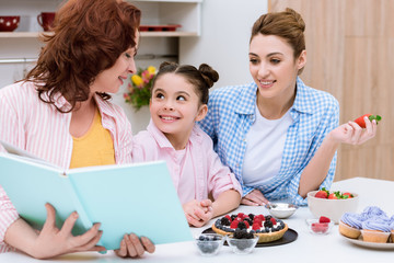 three generations of women reading recipe book together at kitchen