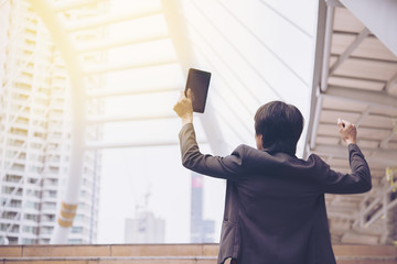 Happy successful businessman holding tablet and outstretched arms,hold hand up and celebrating with his victory in front of the city.businessman successful concept