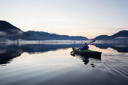 Adventurous Girl kayaking in a beautiful lake during a vibrant sunrise. Taken in Stave Lake, East of Vancouver, BC, Canada.