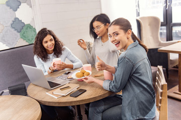Fuel for brain. Happy merry three students visiting cafe while using laptop and laughing