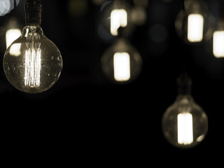 Filament antique looking light bulbs or lamps hanging from ceiling against black background