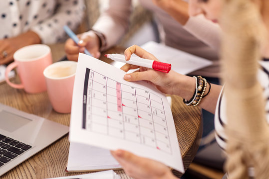 According to plan. Young smooth female hands carrying calendar while planning agenda and marking with liner
