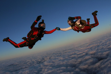 Two skydivers are in the winter sunset sky.